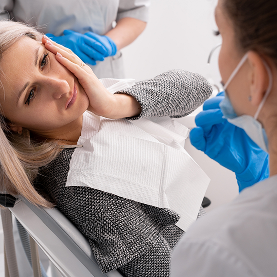 Woman holding her cheek in pain while talking to her emergency dentist in Maplewood