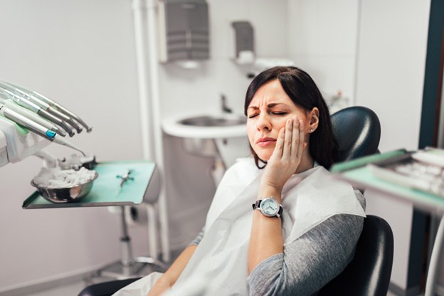 Woman holding her cheek while sitting in dental chair