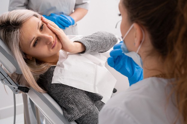 woman looking at dentist holding her cheek in pain