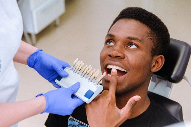 Man in dental chair pointing to teeth with dentist holding up shade guide
