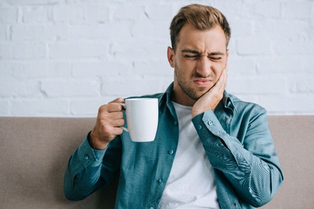 Man holding white mug and touching jaw squinting in pain